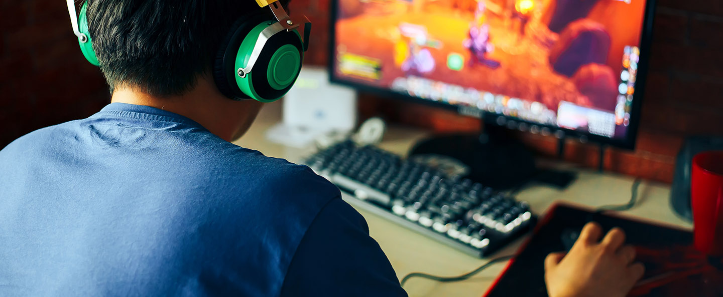 Boy wearing headphones playing a computer games with a mouse and keyboard