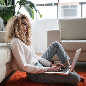 young woman sitting on the floor of her apartment with laptop