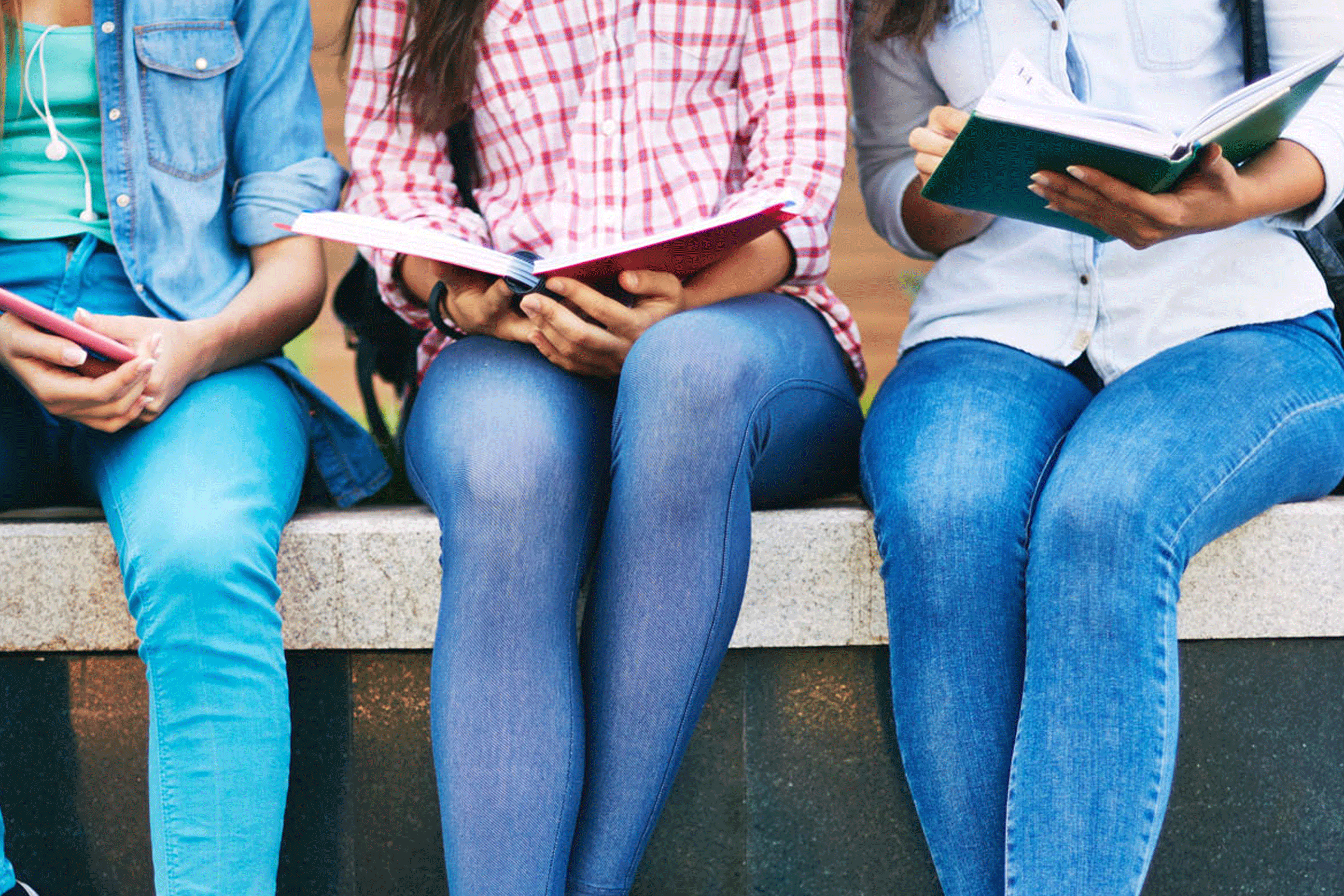 three teenage girls sitting on a ledge reading books for the Bookmans 1317 Club signup