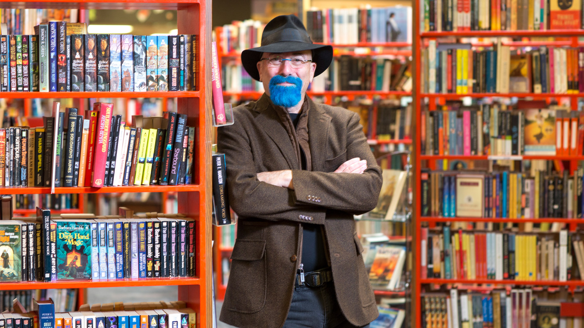 picture of Bookmans owner Bob Oldfather standing in a Bookmans bookstore with a fedora on and a blue goatee