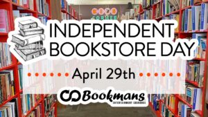 Background of orange floor to ceiling bookshelves. Filled with books. In foreground, stack of books with "Independent Bookstore Day April 29th Bookmans black snake/recycle logo and "Bookmans" in black
