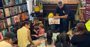A firefighter reads from a picture book to a group of children with their parents