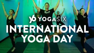 Five people in black, facing front, doing yoga against teal backdrop in background. "Y6 Yoga Six International Yoga Day" In white print in foreground