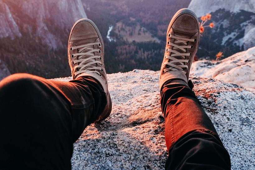 person laying near a cliff with converse on