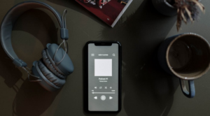 banner event image. In the image there is a pair of over the ear headphones, a coffee cup, and a iphone opened up to a Podcast.