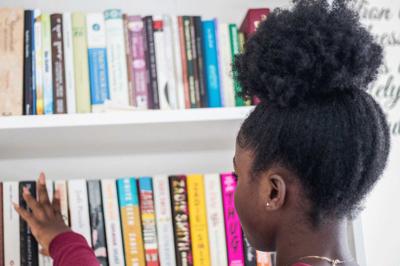 Black African-American little girl looking at books on bookshelf selecting a book